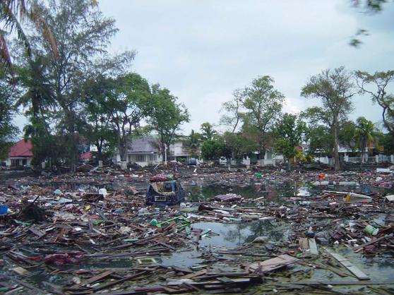 Trash and debris line the streets near local homes in downtown Banda Aceh, Sumatra, after a powerful tsunami swept through the area on 26 Dec 2004 (Source: US Navy/Wikimedia Commons)
